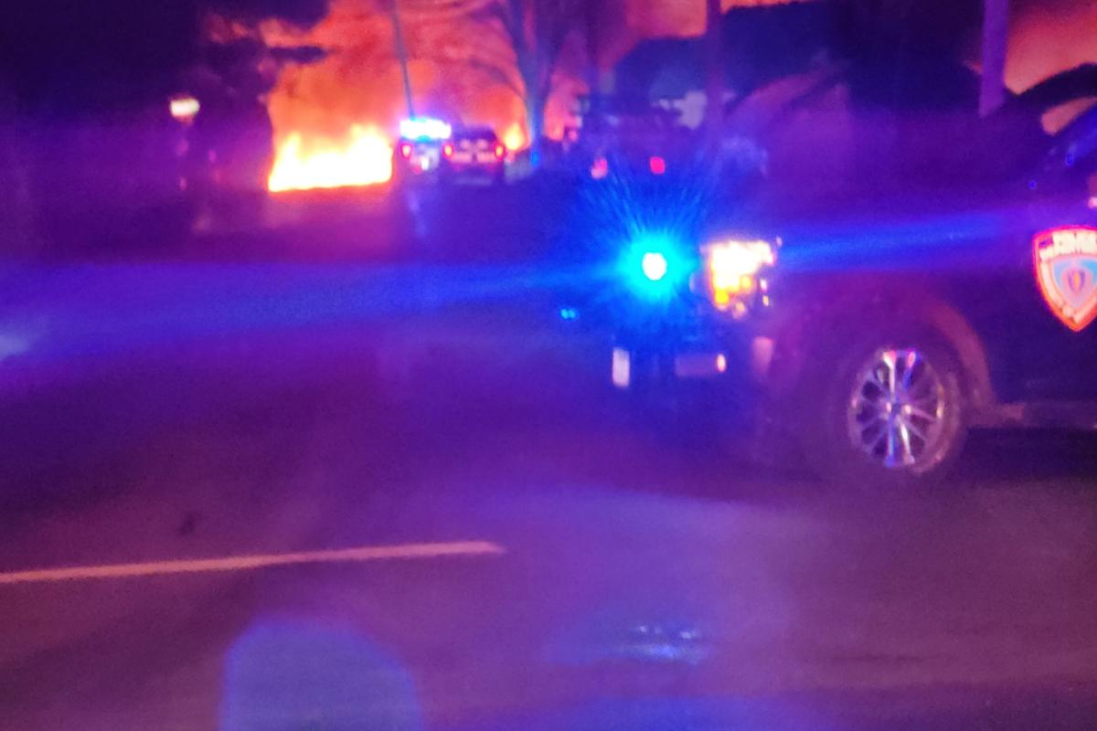 Blue lights flashing from police car as the fire burns in the background.