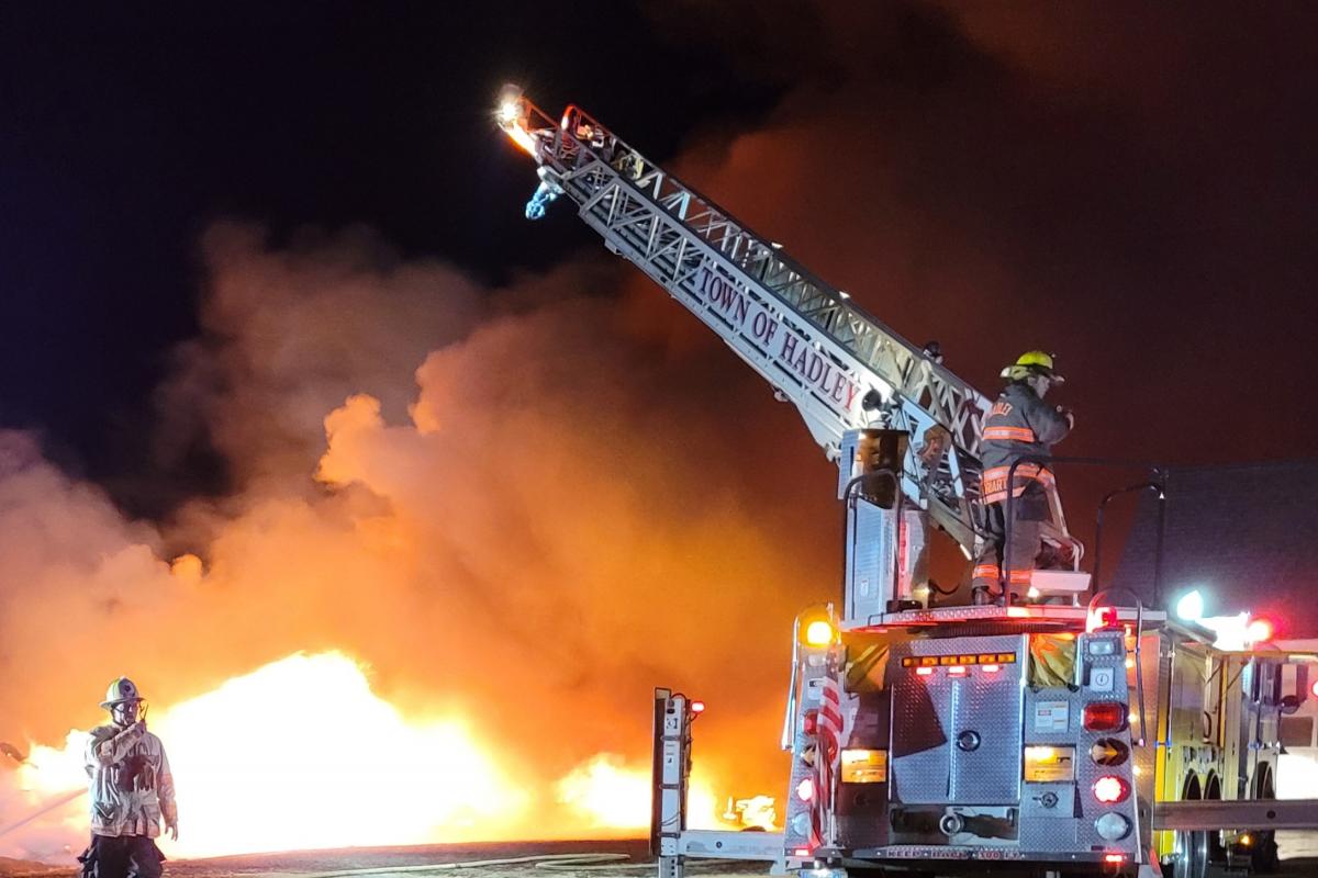 Fully engulfed fire being fought with the engine ladder suspended above fire