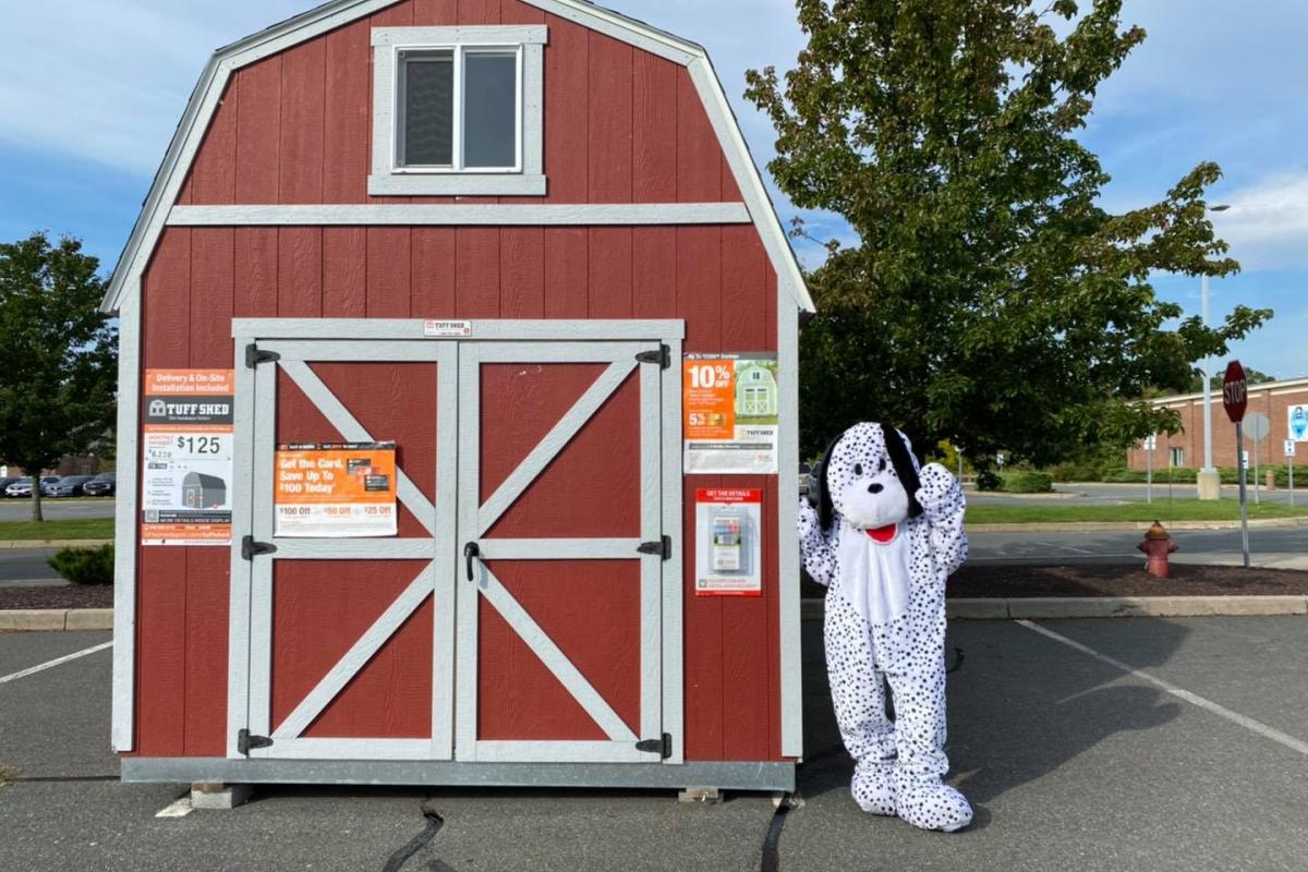 Home Depot's mascot Dalmatian standing and waving beside small barn/shed