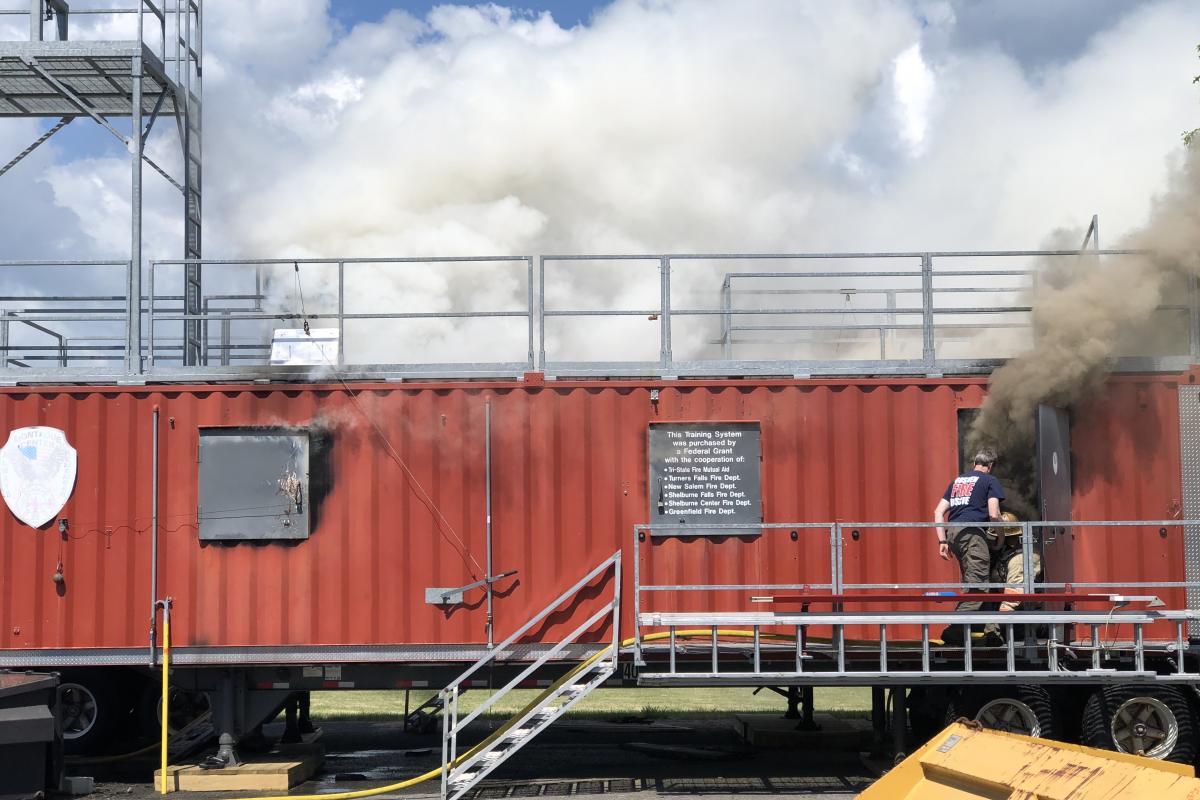 Rear door of red fire training trailer billowing dark smoke